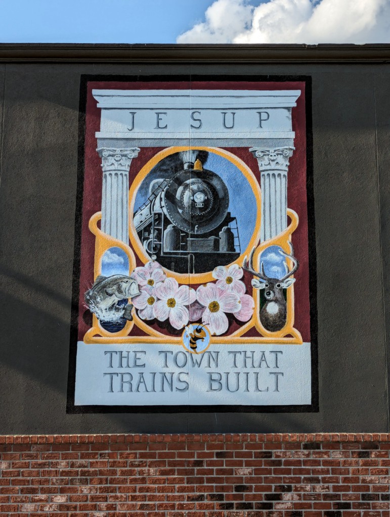 Mural painted on the side of the Pizza Inn in Jesup, GA. Features a train, bass, deer, flowers, and Georgia Tech's Buzz and the words, "Jesup: The Town That Trains Built."
